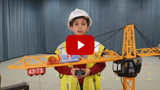 student wearing construction gear standing behind toy crane