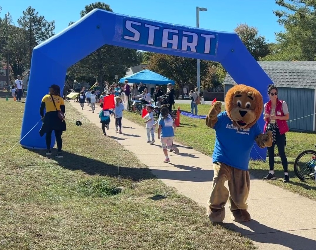 Students running through the Start gate at the Lane Lion Loop Run, with Mr. Paws cheering.
