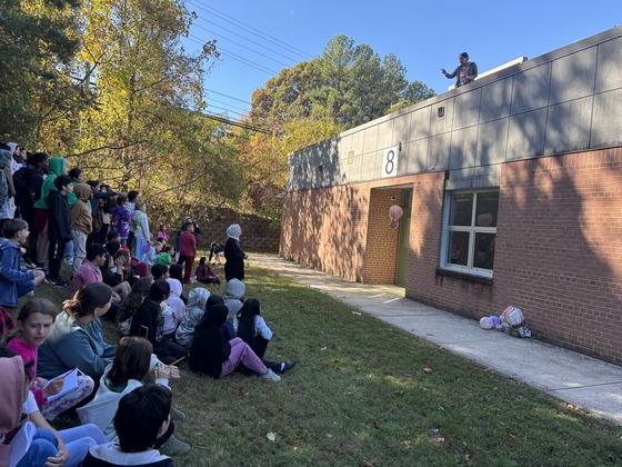 A group of students watch two teachers drop projects from the school roof 