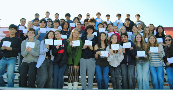 A group of students on bleachers holding certificates and smiling.