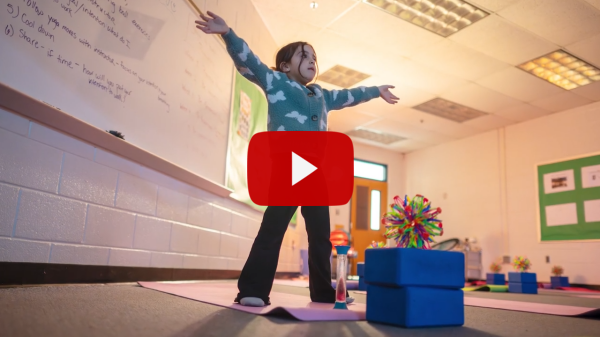 a play button over a girl standing on a yoga mat with her arms spread