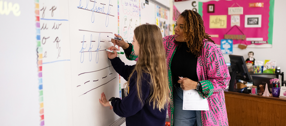 teacher helps student write on whiteboard