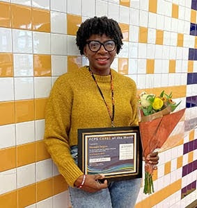 teacher smiling with an award and a bouquet of flowers