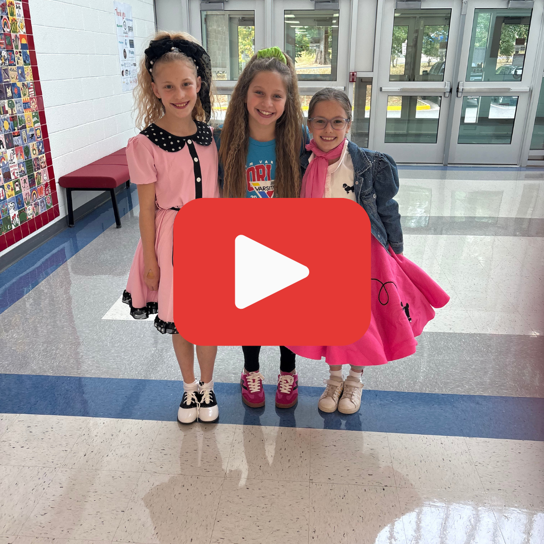 Three young students standing in a school lobby dressed in 70's costumes
