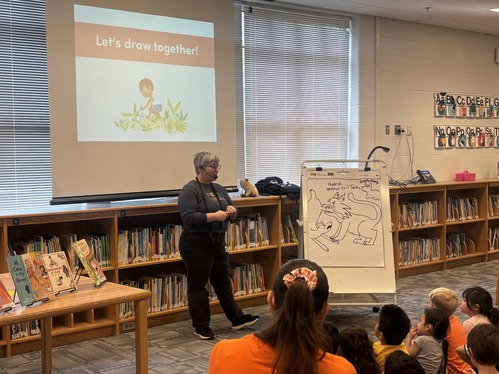 Author stands in front of library demonstrating how she illustrates 