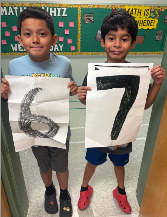 Two boys hold up a 6 and a 7 