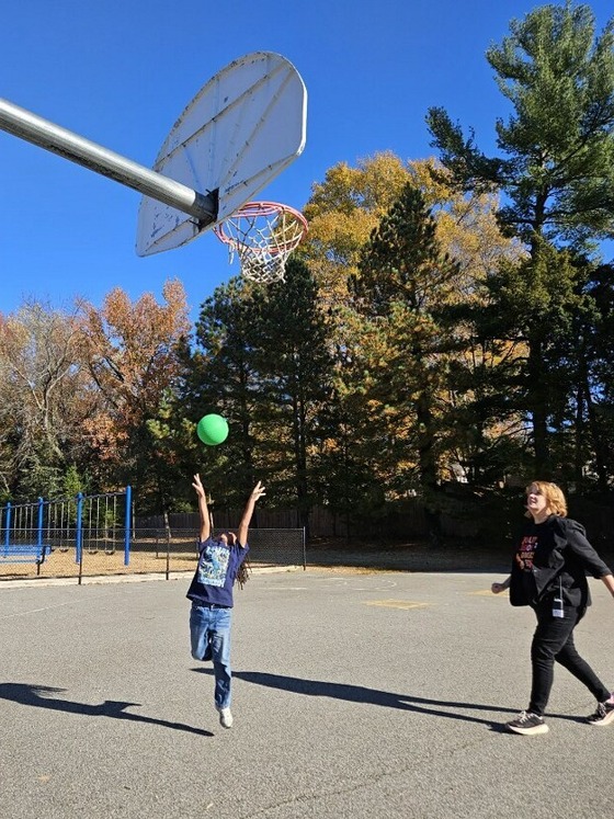 Student playing basketball with teacher.