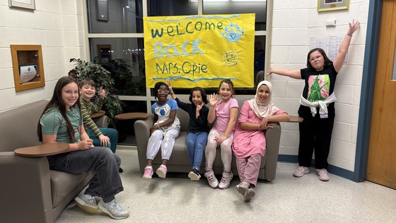Student Ambassadors show off their "Welcome Back, Mrs. Opie!" banner outside the office