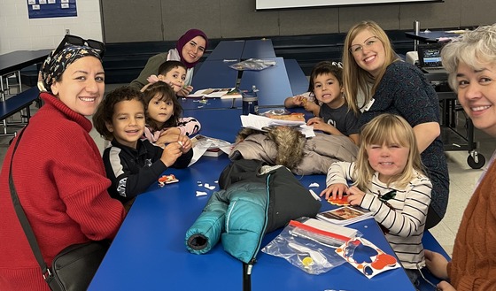PreK families sitting at tables in the cafeteria with books and craft supplies
