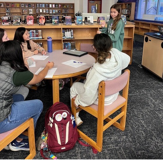 Sitting around table with one student standing