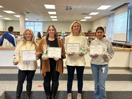 Four teachers stand with certificates in the library 