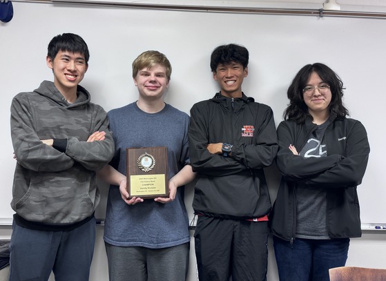 Four students pose with a plaque in front of a dry erase board