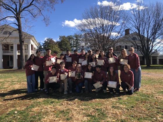 Students, club sponsors, and teachers pose with certificates in front of a colonial style house.
