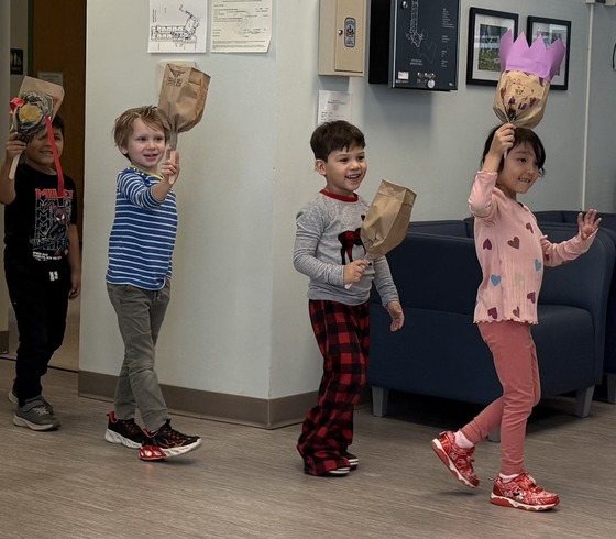 Kindergarten students walk through the office displaying a paper bag craft 