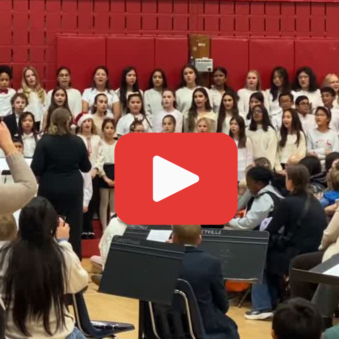 A school choir singing in front of a crowd of families with a large red PLAY button overlayed