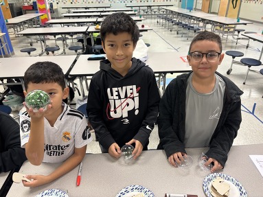 Three boys hold ornaments they made 
