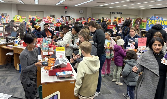 A crowd of shoppers - adults and children - in the library at Book Fair Family Night on 12/3