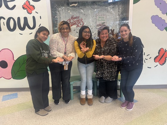 5 teachers pose for a picture while holding a green jingle bell 