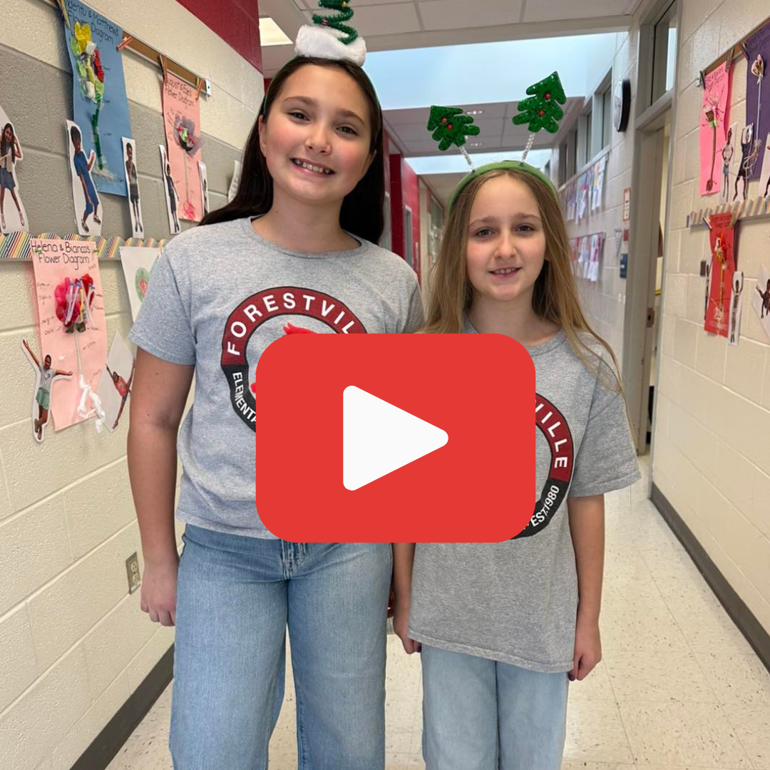 Image of two students in Forestville shirts and holiday headbands smiling in a hallway with a red play button over the image