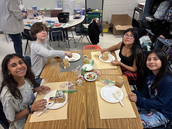 6th grade students smile with their materials to make mini gingerbread houses 