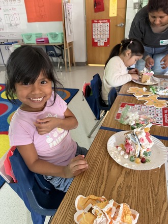 A student smiles while making her Gingerbread house 