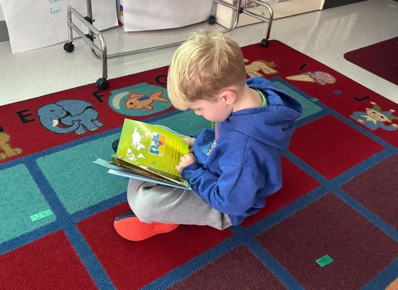 A student sits on the carpet reading a book 