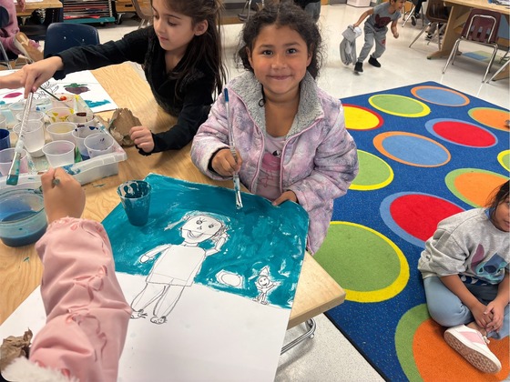 A student smiles while painting a picture in art 