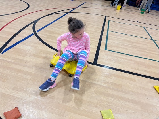 A student sits on a yellow scooter in the gym and moves backwards 