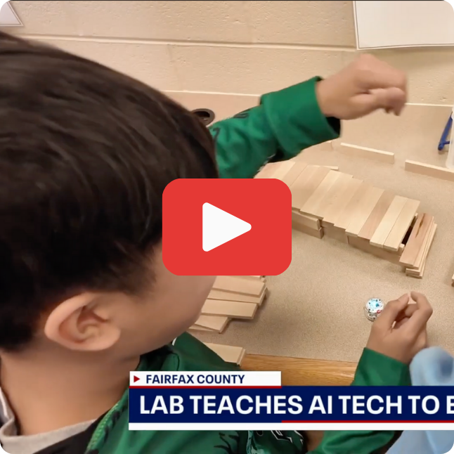 screenshot of news story featuring a student using building blocks and a small robot with lower third on screen and red play button on top