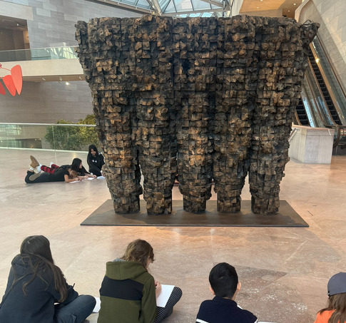 A group of students sit in front of art and draw in their sketchbooks 