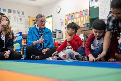 Dr. Reid sitting on floor with Kindergarten students