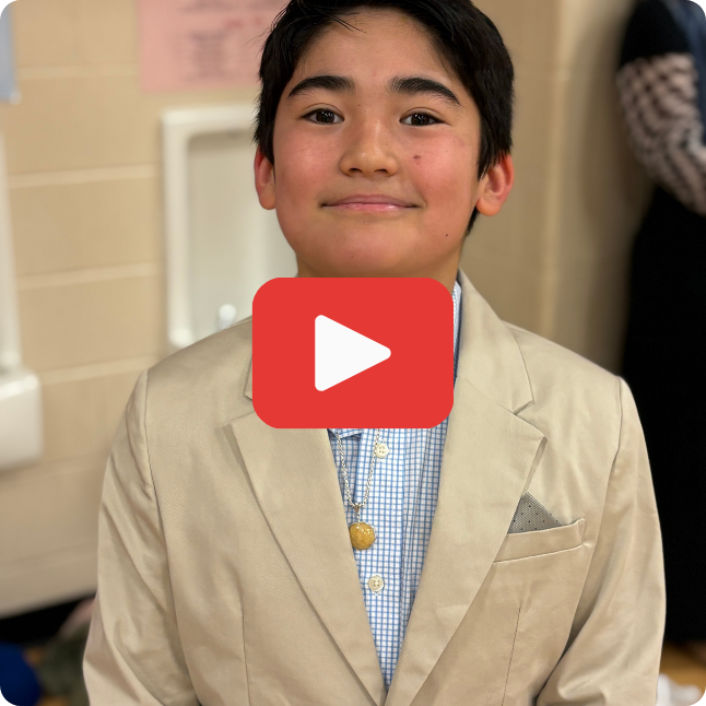 smiling boy wearing cream colored suit with blue button-down collared shirt and red and white play button on top of the image