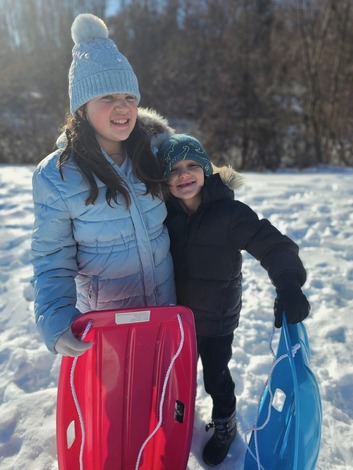 A boy and a girl smile outside in the snow 