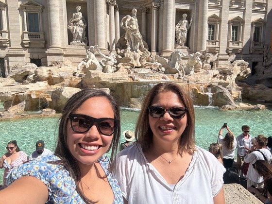 two people take a selfie and smile in front of the Trevi Fountain