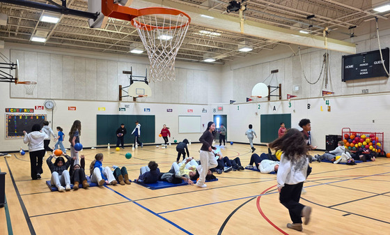 Students participate in activities including floor exercises, basketball, and games with balls and pins inside a school gymnasium.