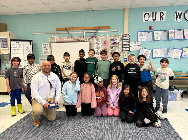 Mrs. Louie's 3rd grade class.  Students standing together with Mr. Marotta kneeling holding the attendance trophy