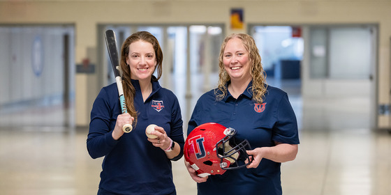 Jennifer Hammond standing on left with baseball bat and ball and Rachel Worsham standing on the right with football helmet.