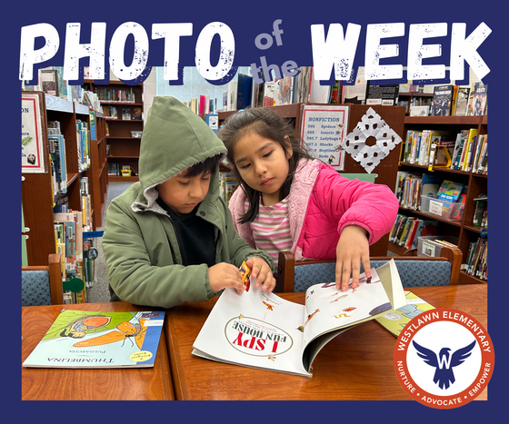 two students look through a book in the library