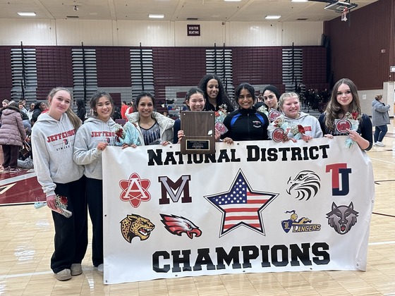 Gymnastics team poses with National District Championship banner.