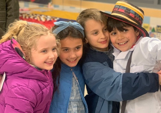 Four smiling children embrace during CultureFest in the background there are international displays.