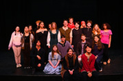 A group of 21 high school students pose in a photo on stage in front of a black background