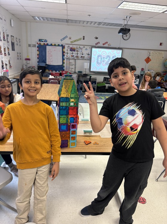 Two students posing in front of a tower built of magnetic tiles