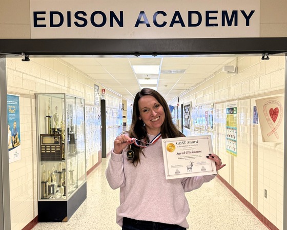 Teacher in hallway holding an award under the Edison Academy sign