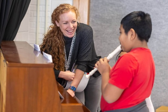 teacher smiles at student while student plays the recorder