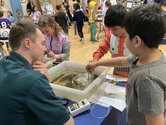 students looking at table at career fair with container of river water