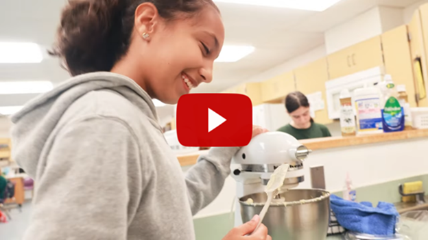 Student standing in front of mixer while holding spatula