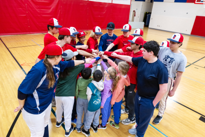 Baseball players and children standing in circle with arms extended
