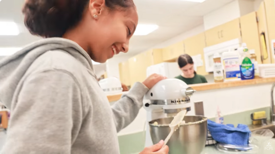 A smiling student makes batter with a mixer in a home economics classroom