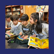 students sit cross-legged with open books in their laps, their eyes focused on each other's books