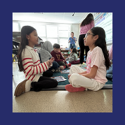 two students sit on the floor facing each other, engaged in conversation